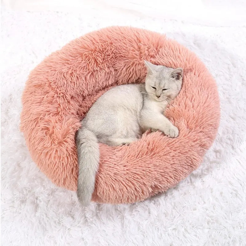 Plush round pet bed in pink with a cat lying inside.